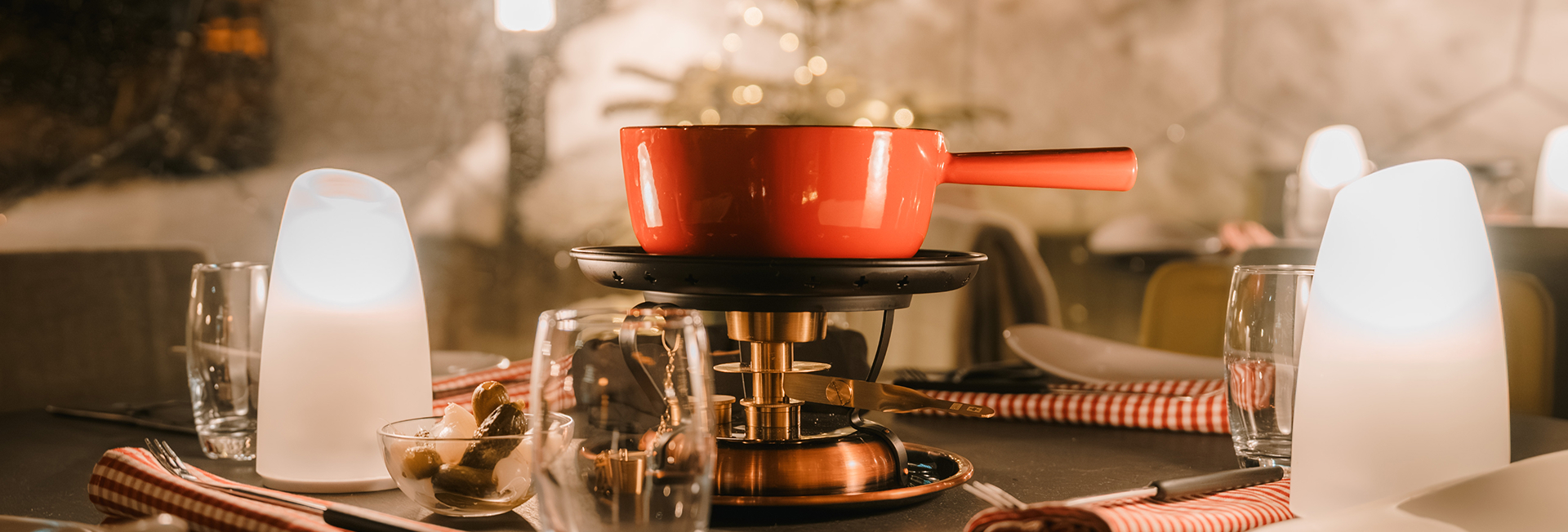 Roter Fondue-Topf auf einem Rechaud, serviert auf einem stilvoll gedeckten Tisch mit warmer Beleuchtung im Hotel Ambassador Zermatt.