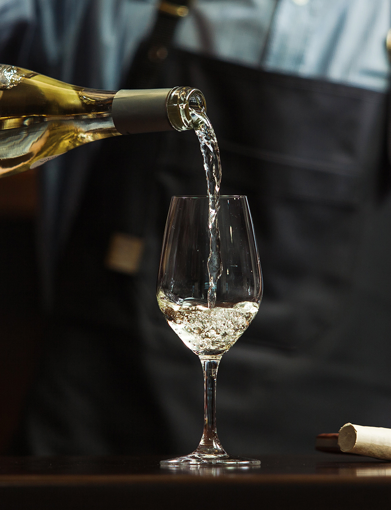 Male sommelier pouring white wine into long-stemmed wineglasses.